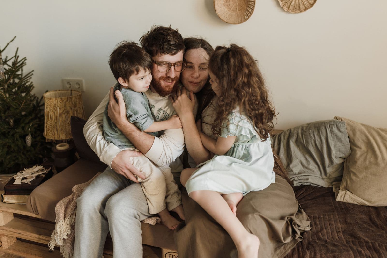 A mother and father hugging their two young children on a couch at home